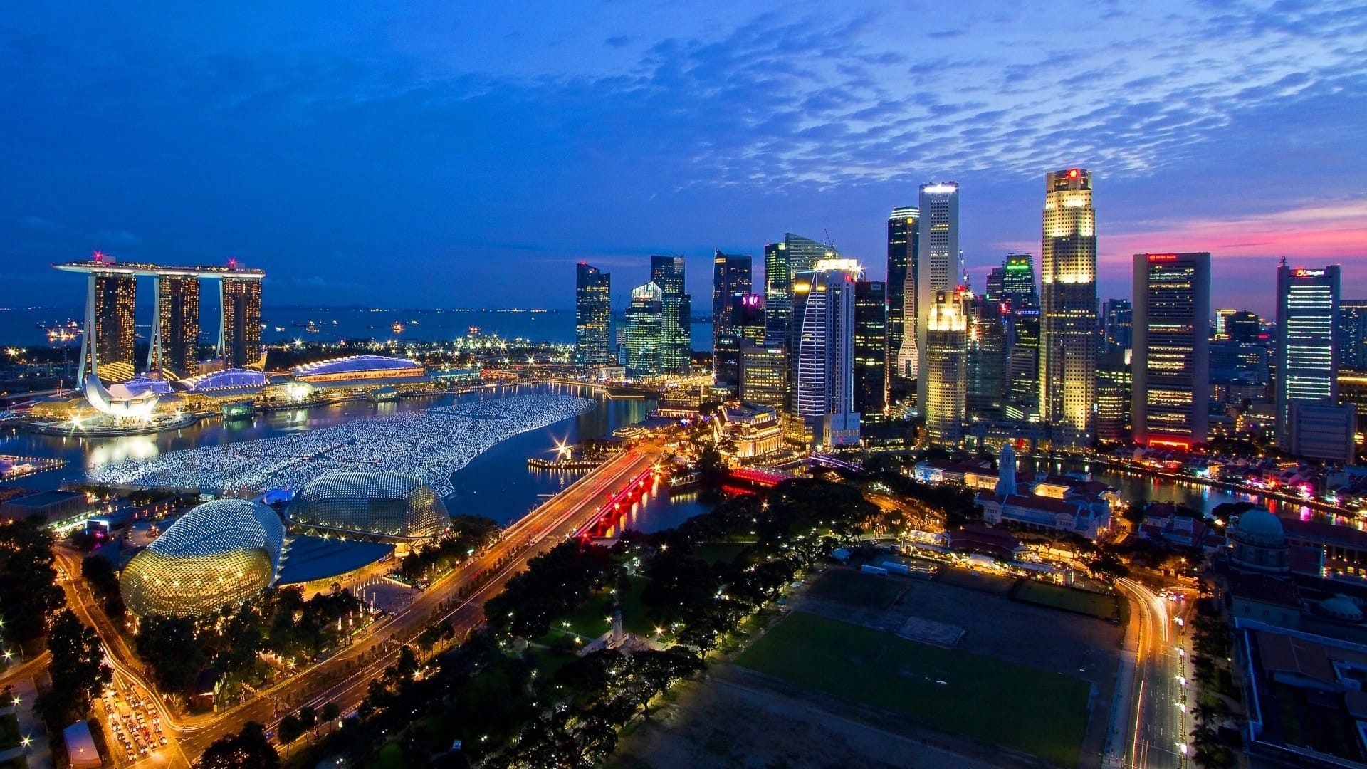 Aerial view of Singapore's illuminated skyline at dusk with skyscrapers, Marina Bay Sands, and a glowing waterfront.